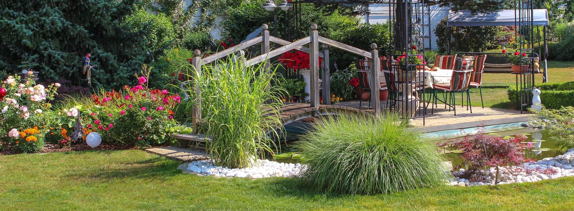 Brücke über Gartengewässer neben Terasse mit Gartenmöbeln